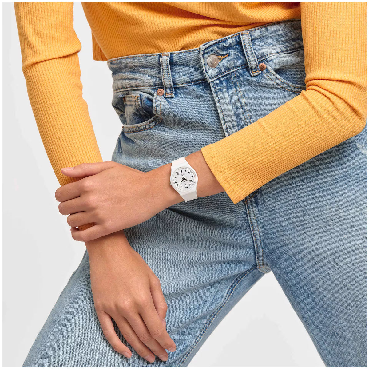 Orologio Swatch bianco indossato al polso, abbinato a una maglia gialla e jeans azzurri.