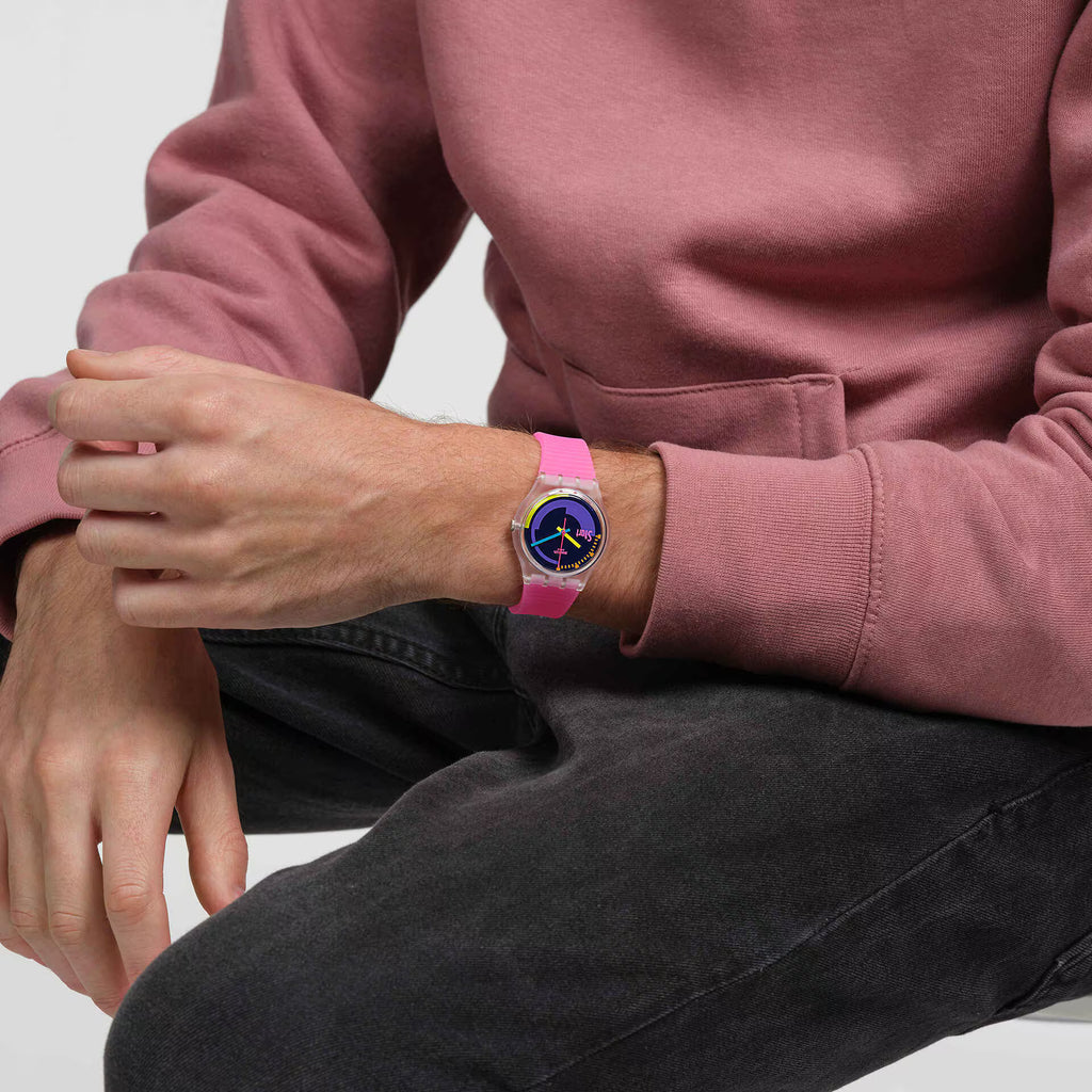 Swatch Neon Pink Podium SO28K111 indossato con felpa rosa e jeans scuri, dettaglio della cassa trasparente e del cinturino rosa.