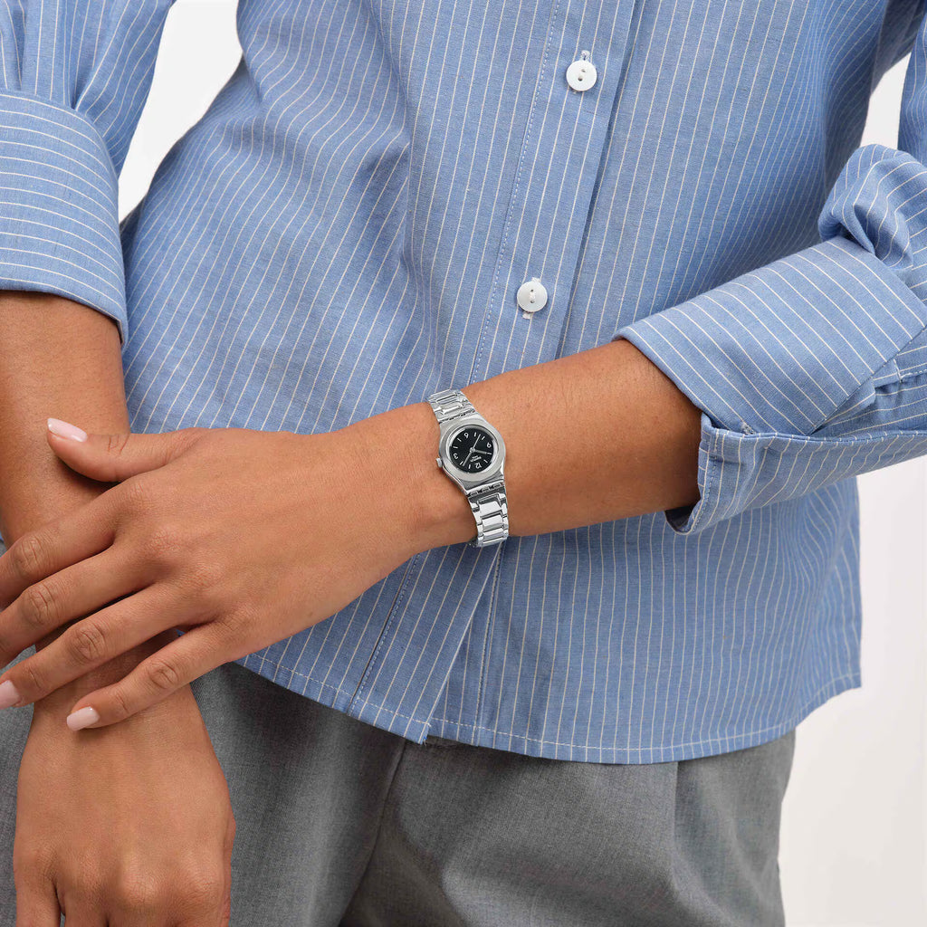 Swatch Irony Gradino Nero YSS350G indossato al polso con camicia azzurra, quadrante nero e bracciale in acciaio.