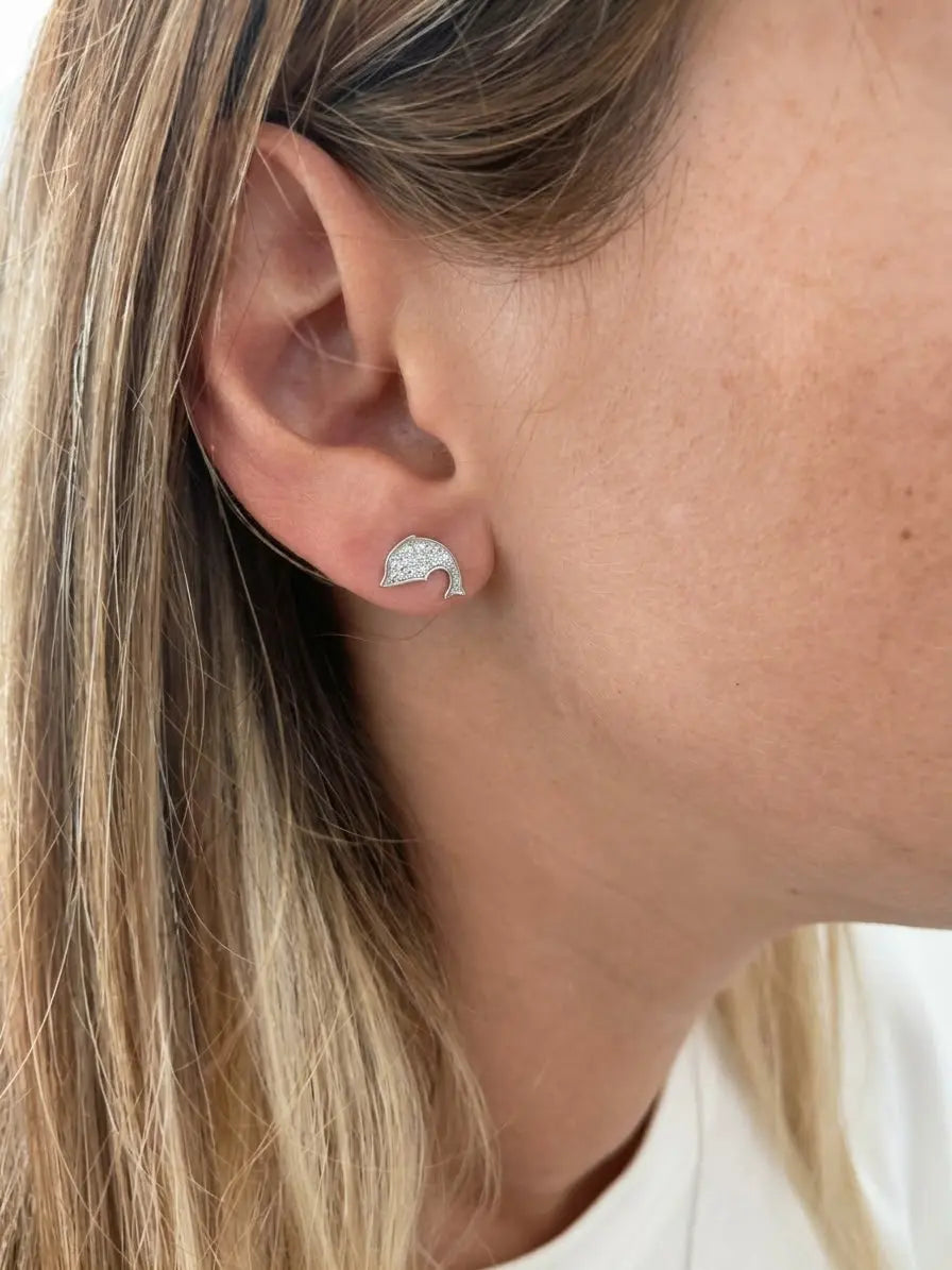 Orecchino a delfino OR0116 indossato al lobo, con zirconi luminosi e capelli scostati dietro l’orecchio.
