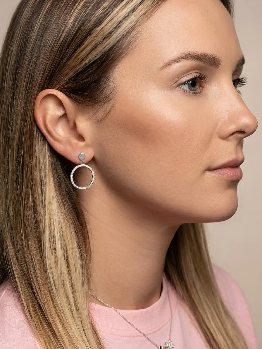 Orecchino OR0133 con cerchio pendente impreziosito da zirconi bianchi indossato, con capelli dietro l’orecchio.