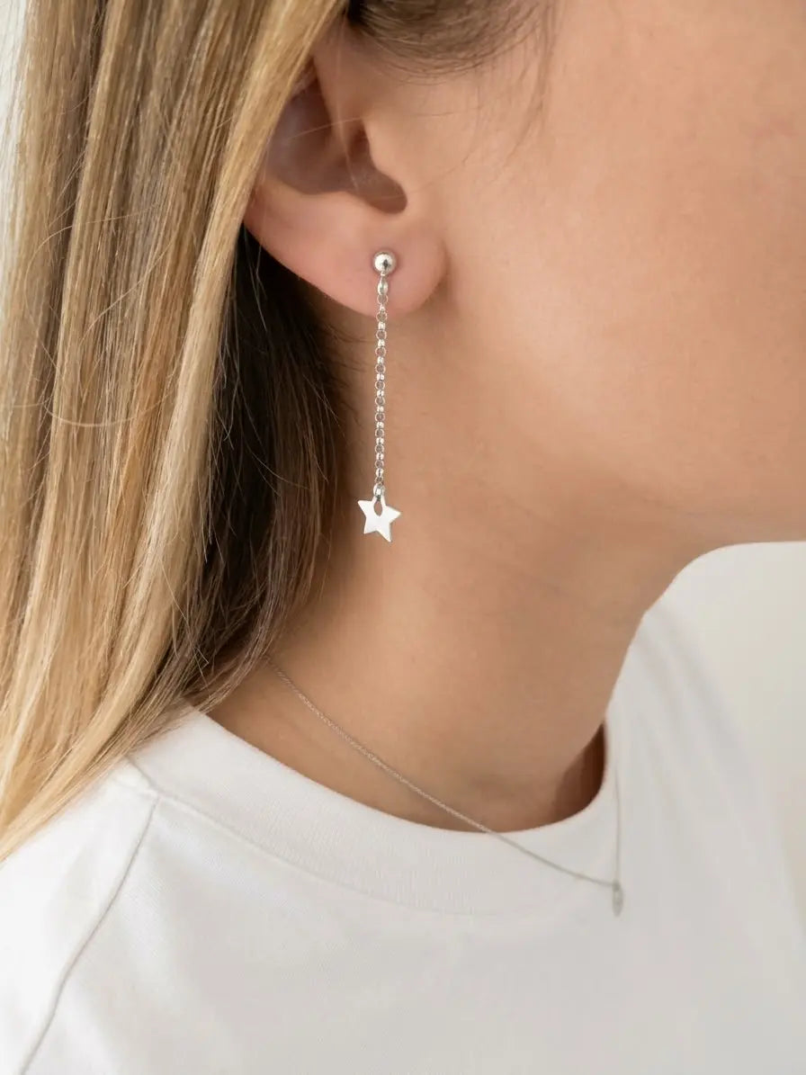 Orecchino pendente OR0155 in argento 925 indossato, con catenina sottile e stella lucida a cinque punte accanto al viso. CICCO Gioielleria.
